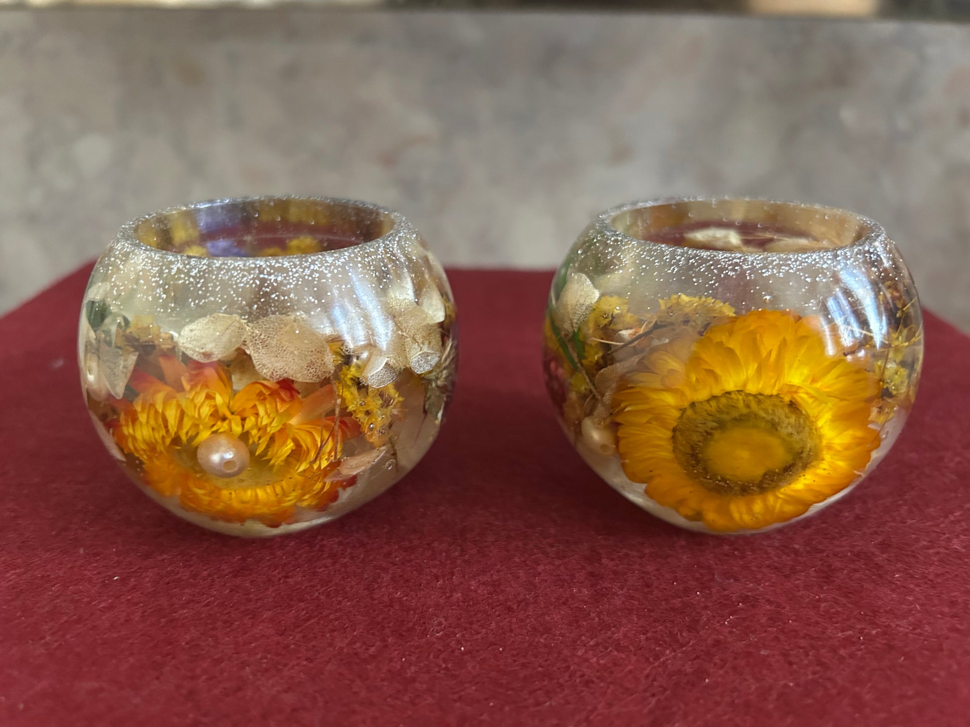 Two glass containers with sunflowers inside on a red surface.