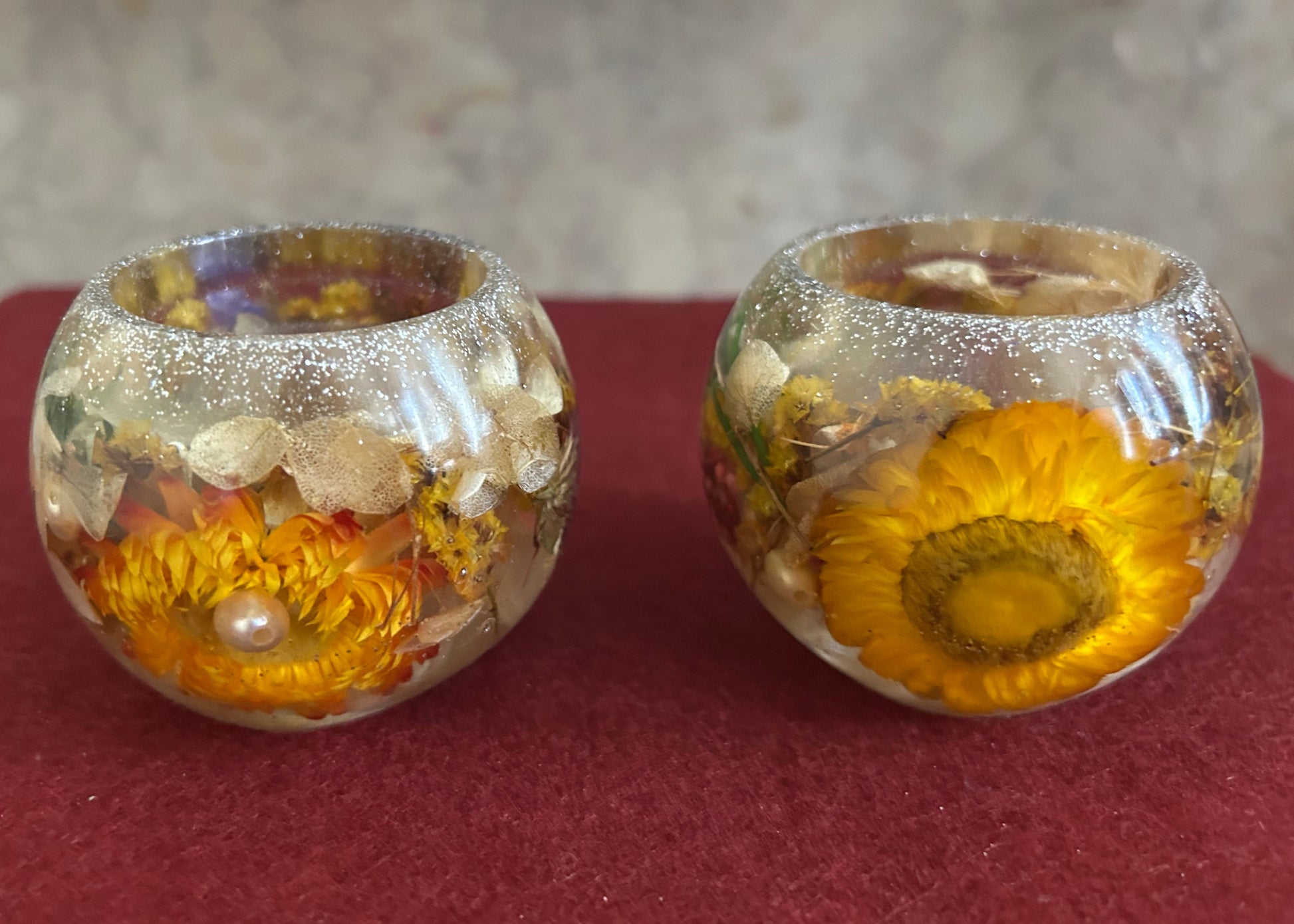 Two glass candle holders with sunflower designs on a red surface.