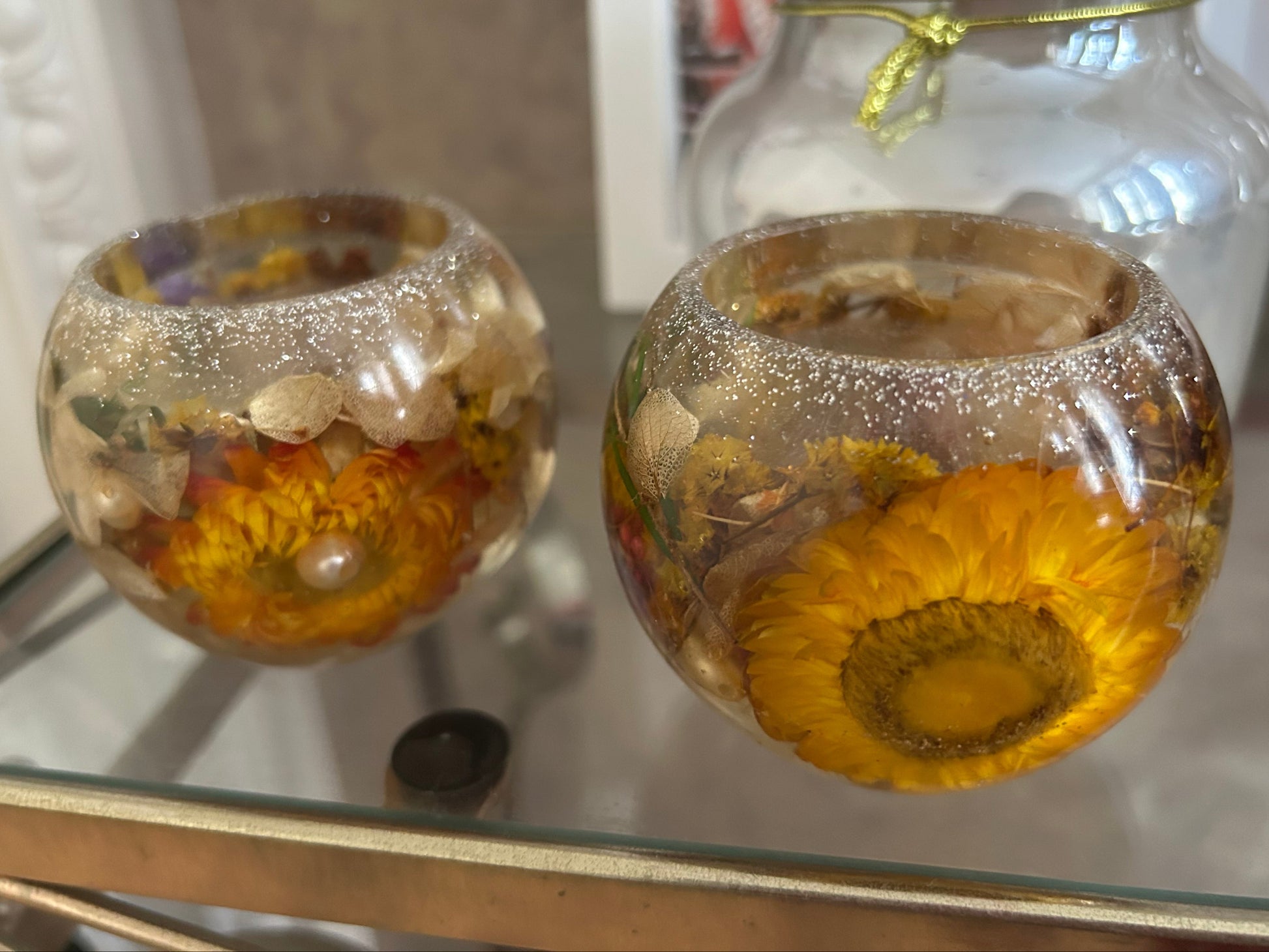 Two glass containers with sunflower heads and decorative elements on a reflective surface.