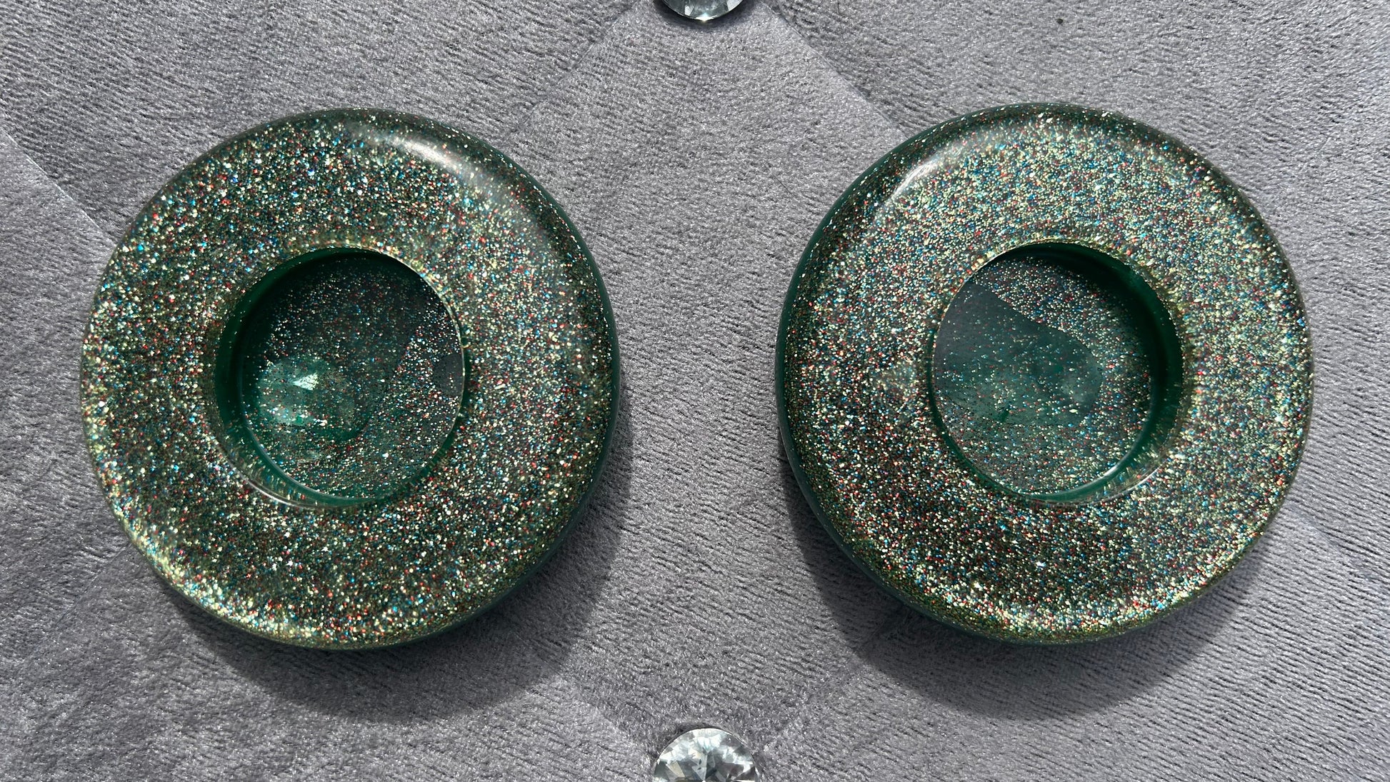 Two green metallic circular objects on a textured gray surface with small crystals around.