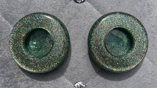Two green metallic circular objects on a textured gray surface with small crystals around.