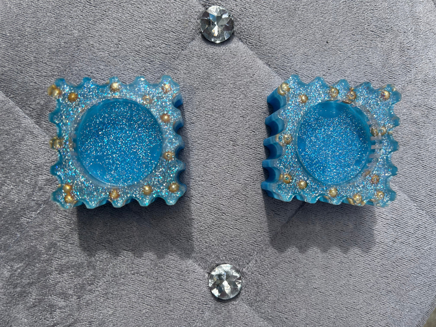 Blue glittery earrings with gold accents on a gray surface.