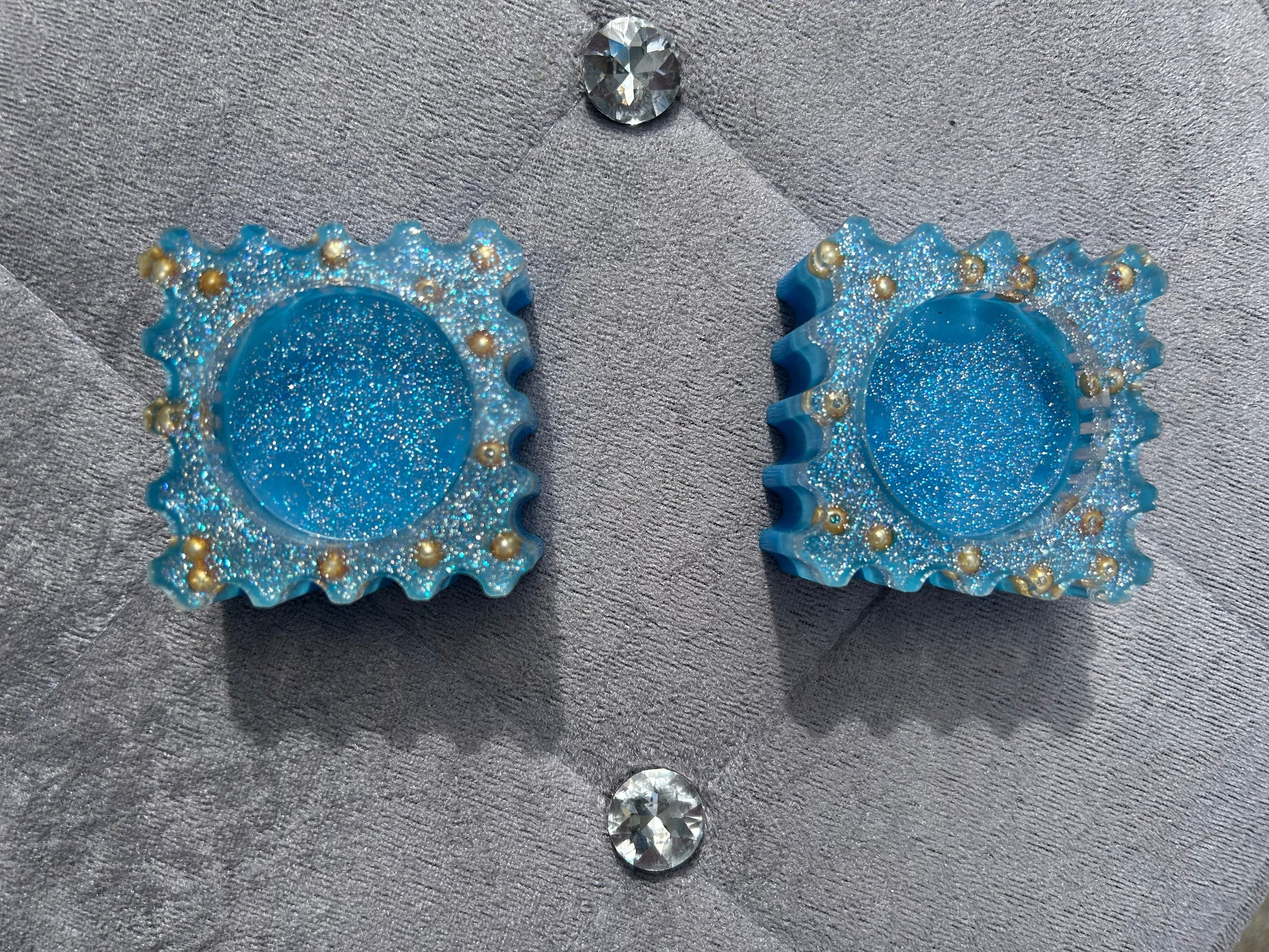 Blue glittery earrings with gold accents on a gray surface.