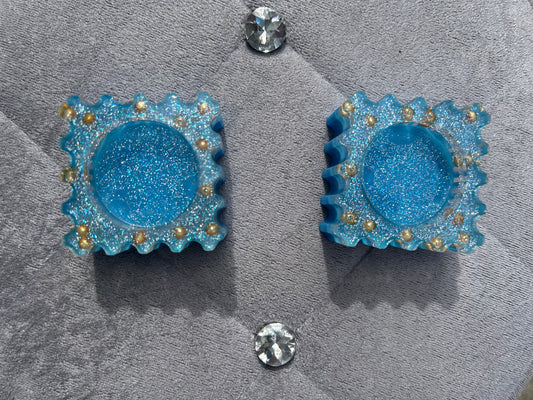 Blue glittery earrings with gold accents on a gray surface.