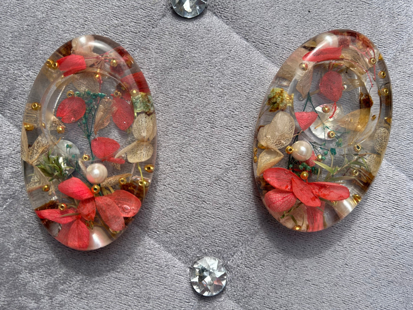 Pair of earrings with floral and pearl design on a textured surface