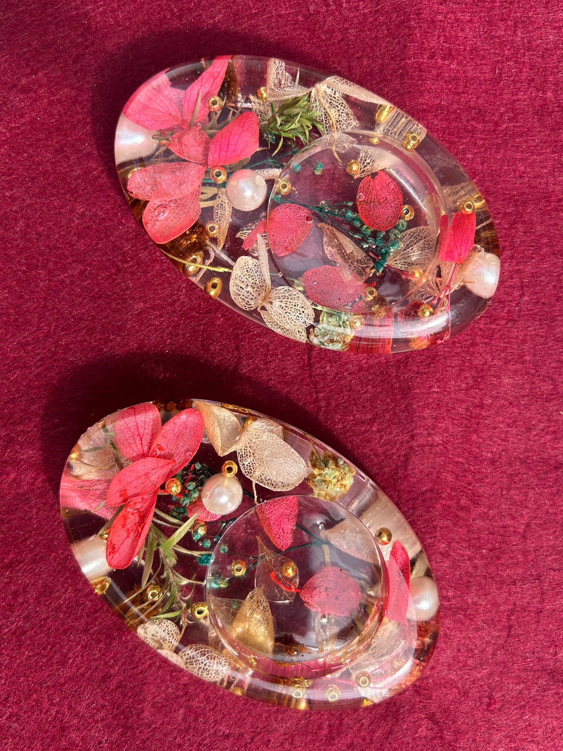 Pair of floral earrings with pink flowers and green leaves on a red background