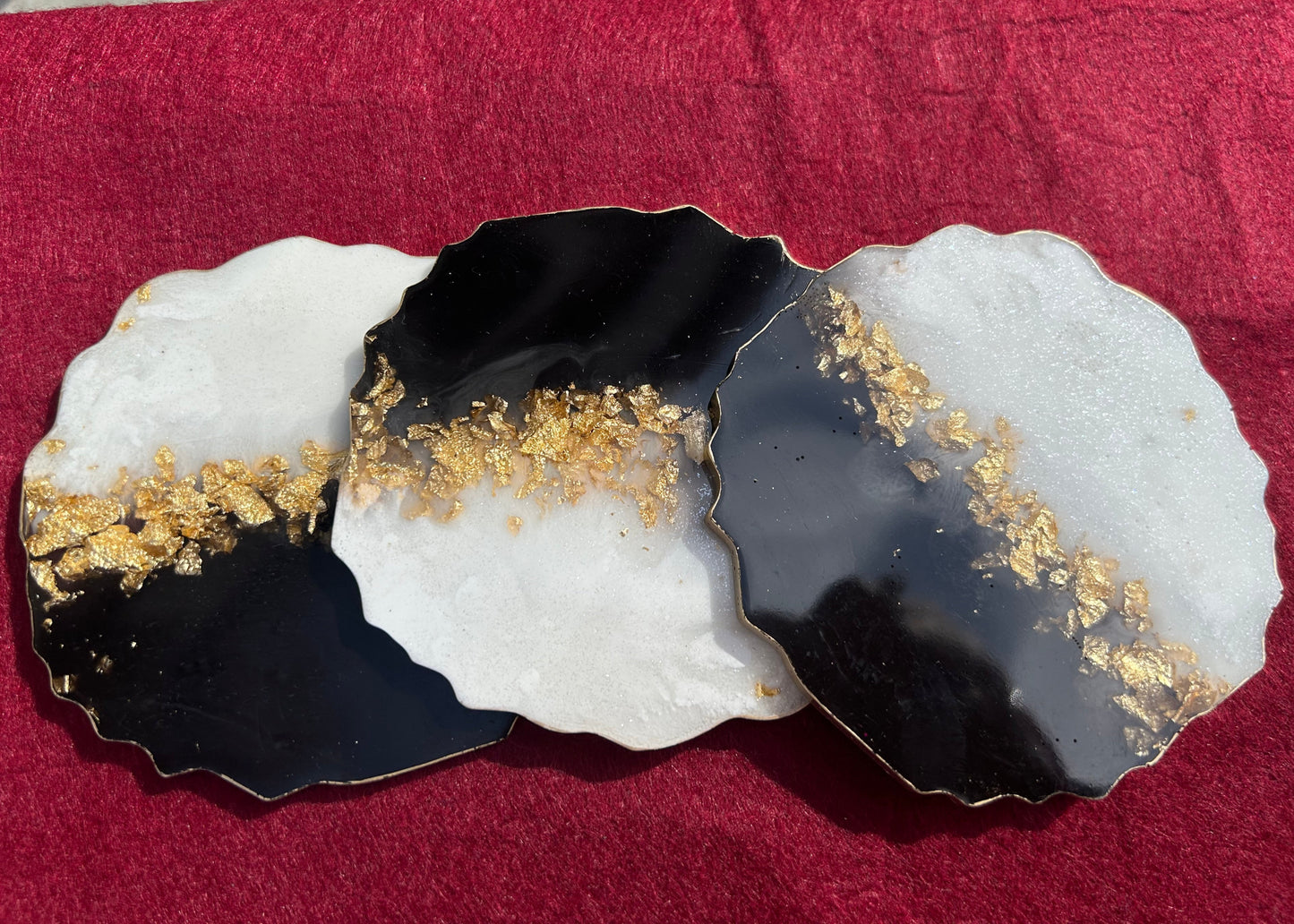 Three decorative coasters with black, white, and gold design on a red surface.