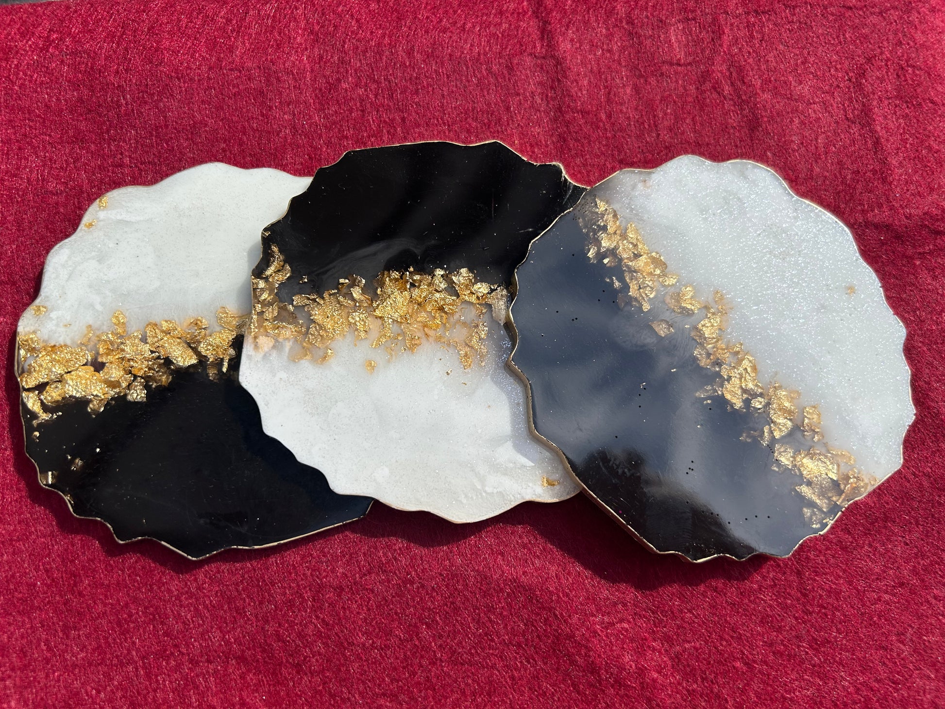 Three decorative coasters with black, white, and gold design on a red fabric background