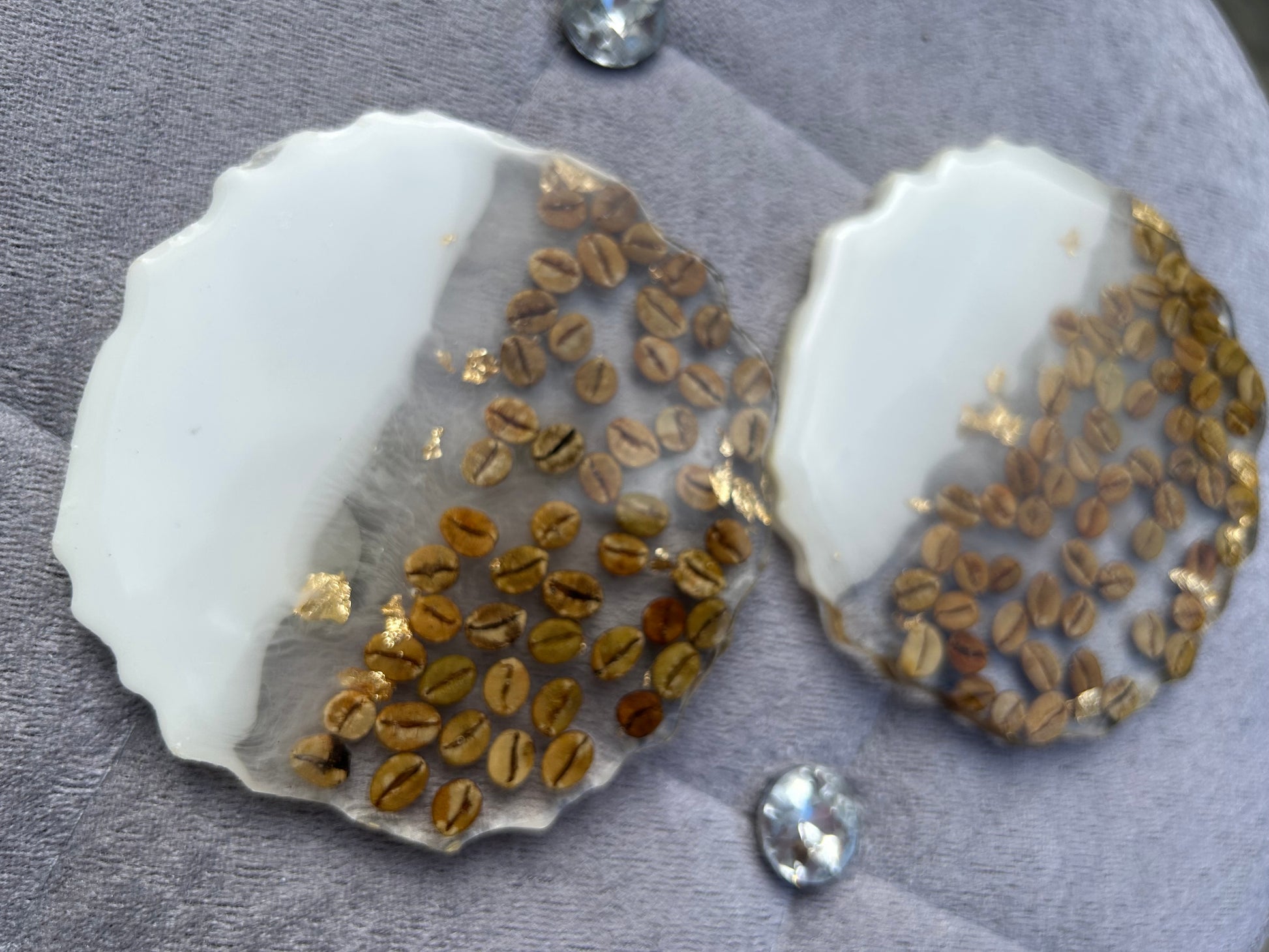 Two seashells with embedded gold and brown seeds on a gray surface.