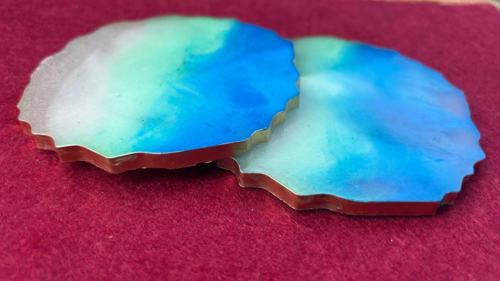 Two blue and green ceramic coasters on a red surface