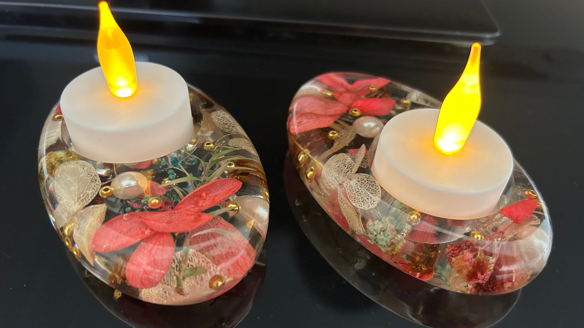 Two decorative candles with floral elements and glowing yellow flames on a reflective surface.
