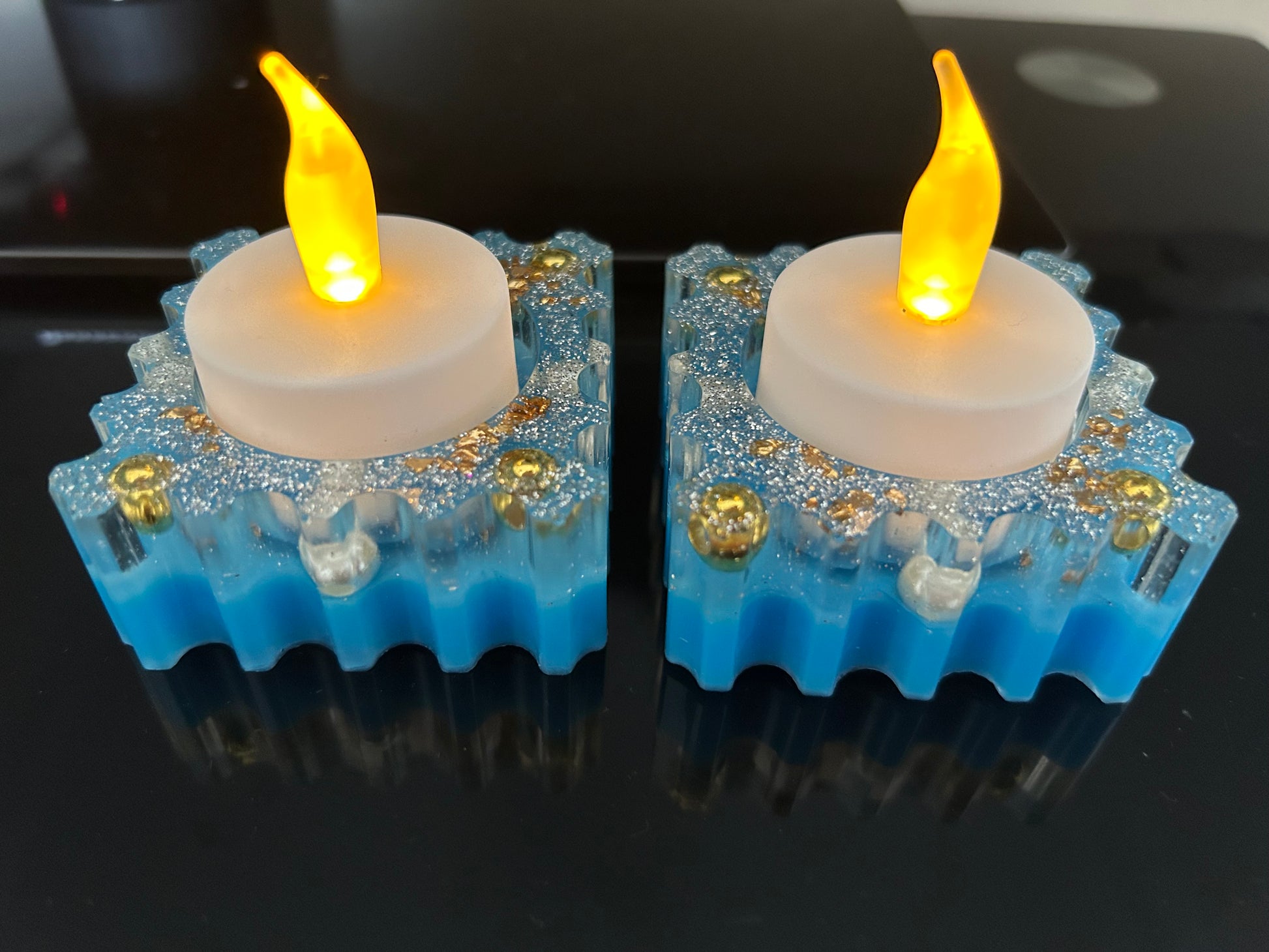 Two LED candles with blue bases and gold accents on a reflective surface.