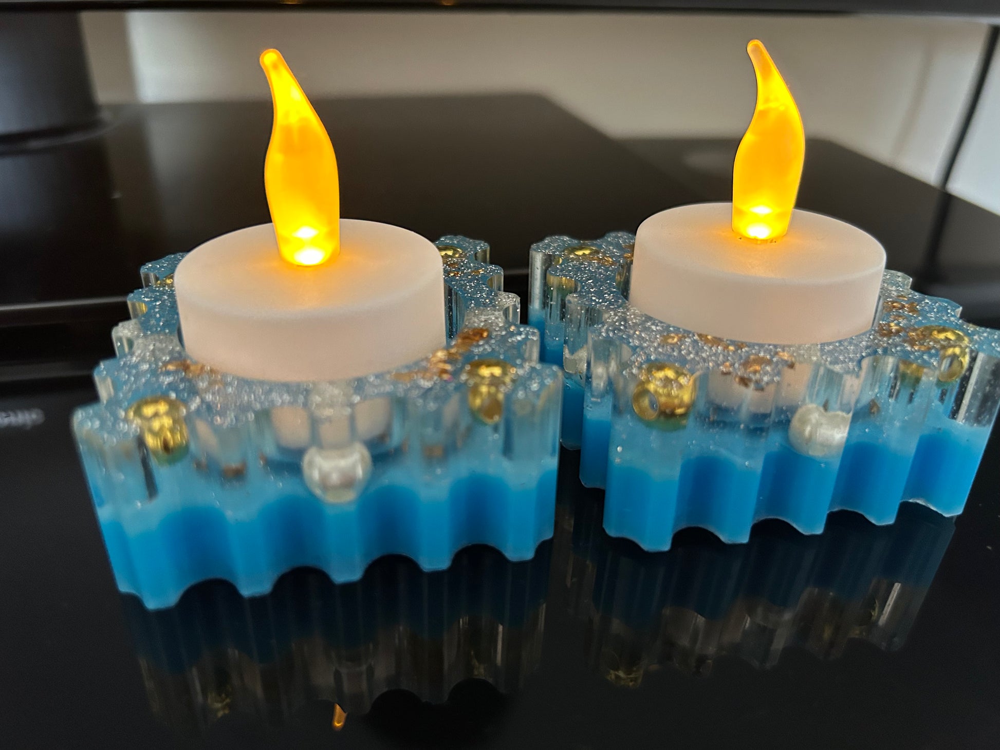 Two LED candles with blue bases on a reflective surface.