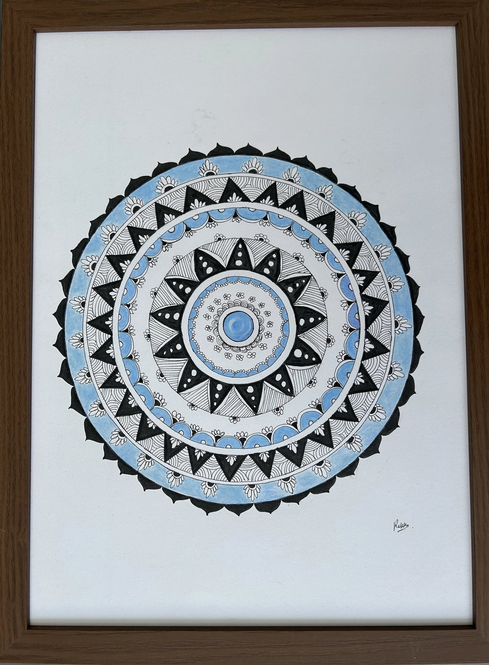 Framed mandala art with concentric circles in black, blue, and white on a white background.